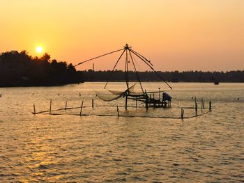 Silhouette a chinese fishing net  in sea against sky during sunset