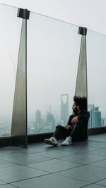 Side view of man sitting on floor against sky