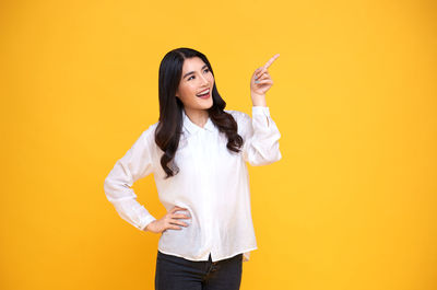 Portrait of smiling young woman against yellow background