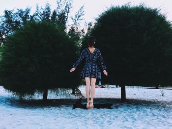 Rear view of woman levitating over sand against trees