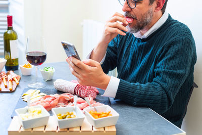 Midsection of man holding mobile phone while sitting on table