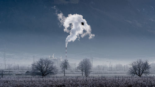 Smoke emitting from chimney on field against sky