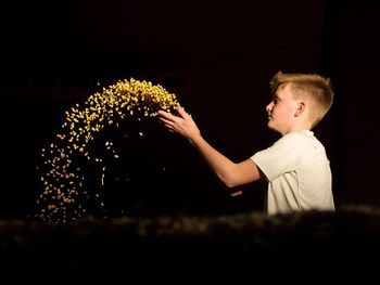 Boy throwing corn on field against sky at night