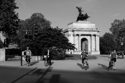 People with bicycles on street against wellington arch in city