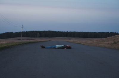 Man lying on road against sky