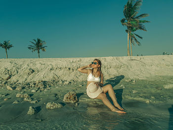 Full length of young woman sitting on beach against sky