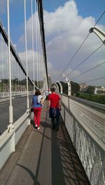 Rear view of woman standing on bridge against cloudy sky