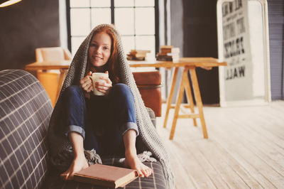 Portrait of young woman holding mug while sitting on sofa at home