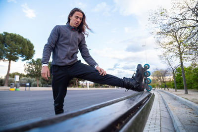 Young man wearing roller skates stretching on bench