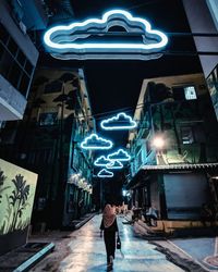 Rear view of woman walking on illuminated street at night