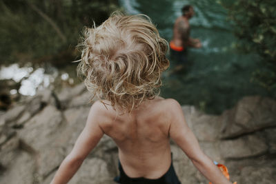 Rear view of shirtless boy looking at father swimming in river