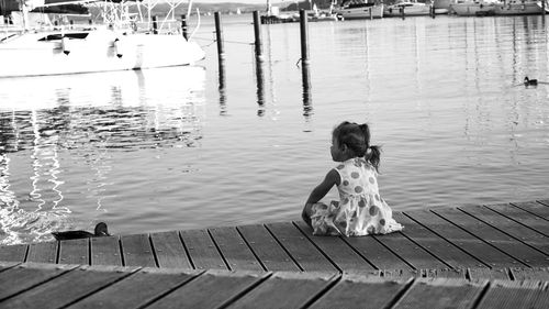 Rear view of girl sitting on pier over lake