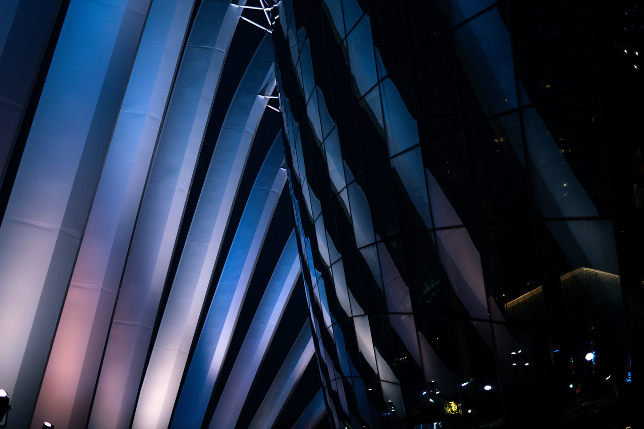 LOW ANGLE VIEW OF ILLUMINATED MODERN BUILDING AT NIGHT