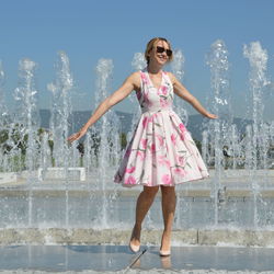 Cheerful woman standing against fountain with arms outstretched