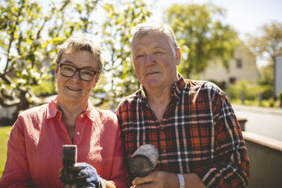 Portrait of confident senior couple holding hammers while standing at yard