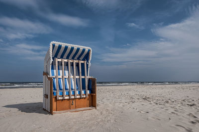 Hooded chair on beach against sky