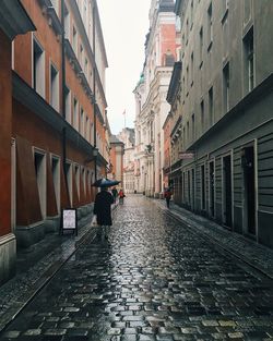 Rear view of people walking down cobblestone street in the rain