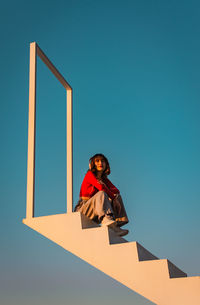 Low angle portrait of woman standing against blue sky