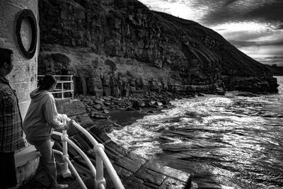 People standing by railing looking at view of sea