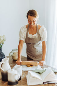 Woman rolling dough for cookies standing at domestic kitchen