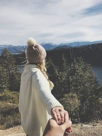 Rear view of woman sitting against mountain and sky