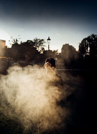 Young man standing amidst smoke on street against sky