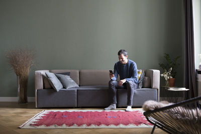 Man sitting on couch in his the living room looking at smartphone