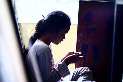 Side view of girl using mobile phone while sitting at home