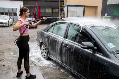 Cute teen girl cleans automobile with foam shampoo chemical detergents during carwash self service