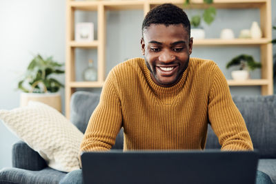 Young man using laptop while sitting on sofa at home