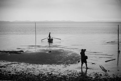 Silhouette photographer photographing man standing on moored boat at beach against sky