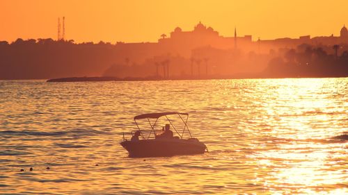 Silhouette sailboat in sea against orange sky