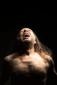 Shirtless aggressive man screaming against black background