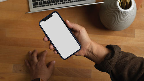 Cropped hand of man holding mobile phone over table