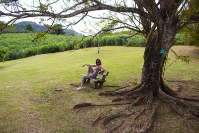 Beautiful young woman sitting on bench under a big tree in martinique, caribbean