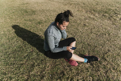 Side view of young woman sitting on grassy field
