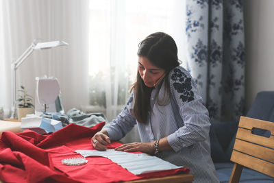 Beautiful woman with long black hair pins the pattern to the fabric and talks on the phone, concept