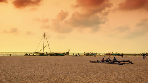 People sitting on sailboat at beach against sky during sunset