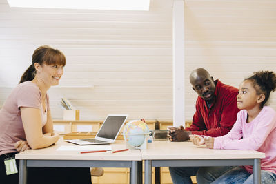 Smiling teacher and man looking at boy during meeting in school