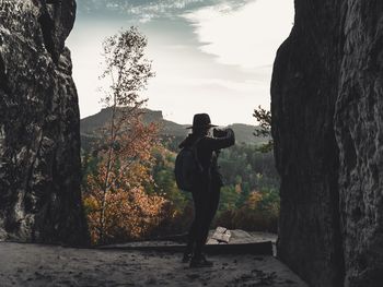 Man photographing by tree against sky