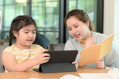 Asian girl studying privately with tutor at home, siblings teaching homework, online learning.