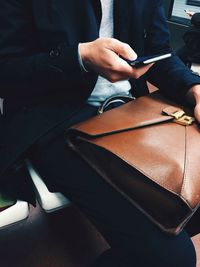 Midsection of businessman using smart phone while sitting with briefcase