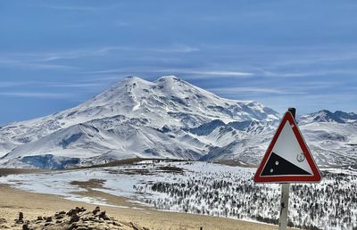 Road sign on snowcapped mountain against sky