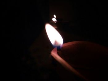 Close-up of hand holding lit candle in darkroom
