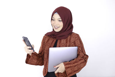 Woman holding smart phone while standing against white background