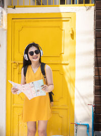 Portrait of smiling young woman standing against yellow door