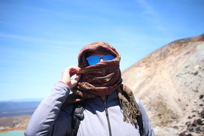 Close-up of man holding wearing scarf against blue sky