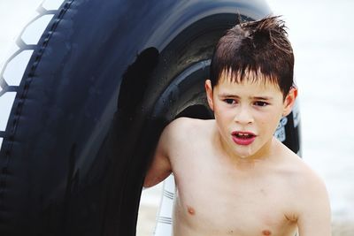 Close-up of wet shirtless boy carrying inflatable ring on beach