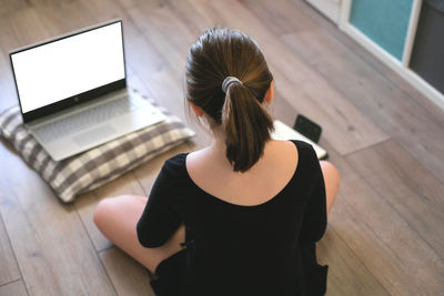 Rear view of girl sitting on floor at home