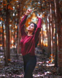 Young woman standing by leaves in forest during autumn
